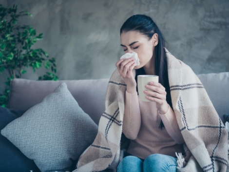 Photo of suffering lady with cup and napkin caught cold drinking medicine from flu covered with blanket, wearing pullover and jeans sitting sofa