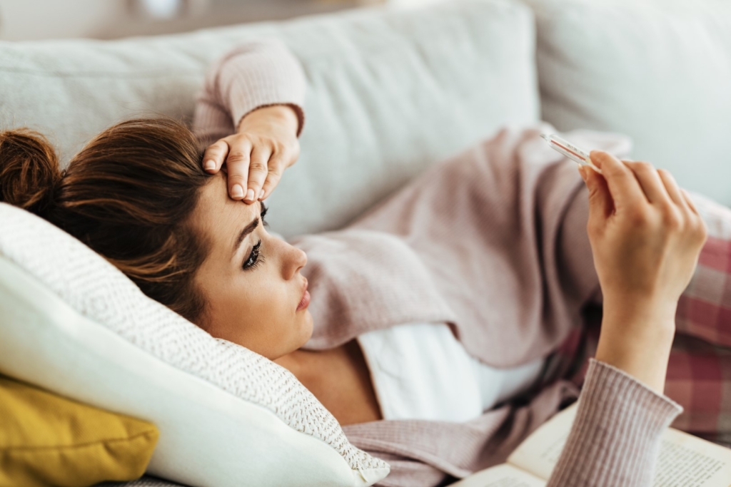Worried woman having high fever while measuring her temperature at home.