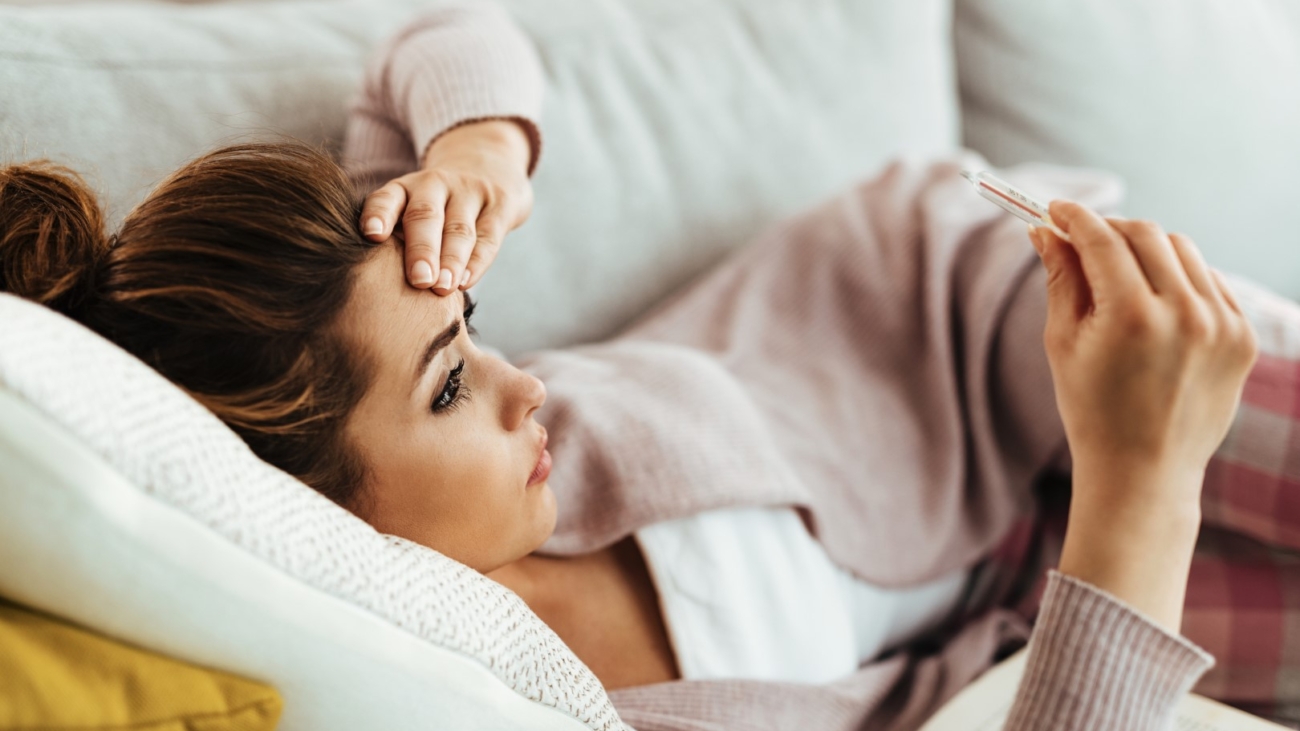 Worried woman having high fever while measuring her temperature at home.