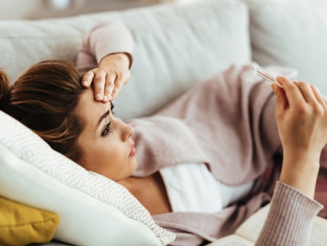 Worried woman having high fever while measuring her temperature at home.