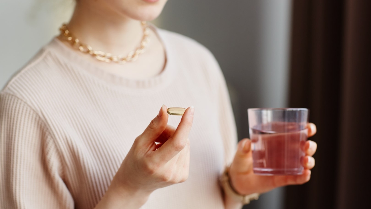 Minimal closeup of young woman holding vitamin capsule while taking supplements with glass of water at home