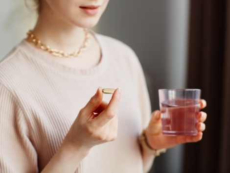 Minimal closeup of young woman holding vitamin capsule while taking supplements with glass of water at home