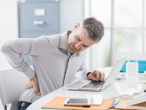 Stressed businessman with backache, he is working at office desk and massaging his back