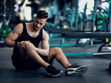 Sport Trauma. Young Arab Male Athlete Touching His Hurted Knee At Gym, Upset Middle Eastern Guy Sitting On Floor And Massaging Sore Injured Leg After Workout Training In Fitness Club, Free Space