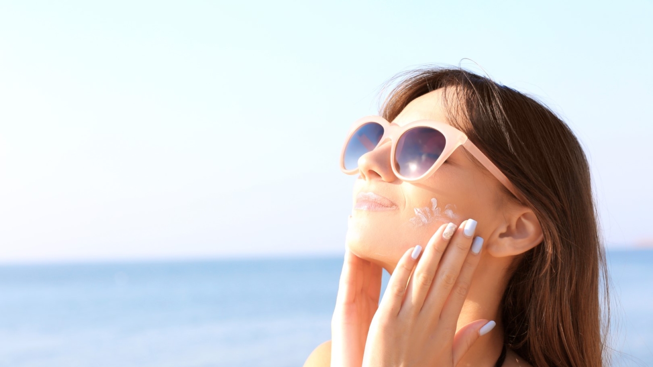 Young woman using sunscreen on the sea background
