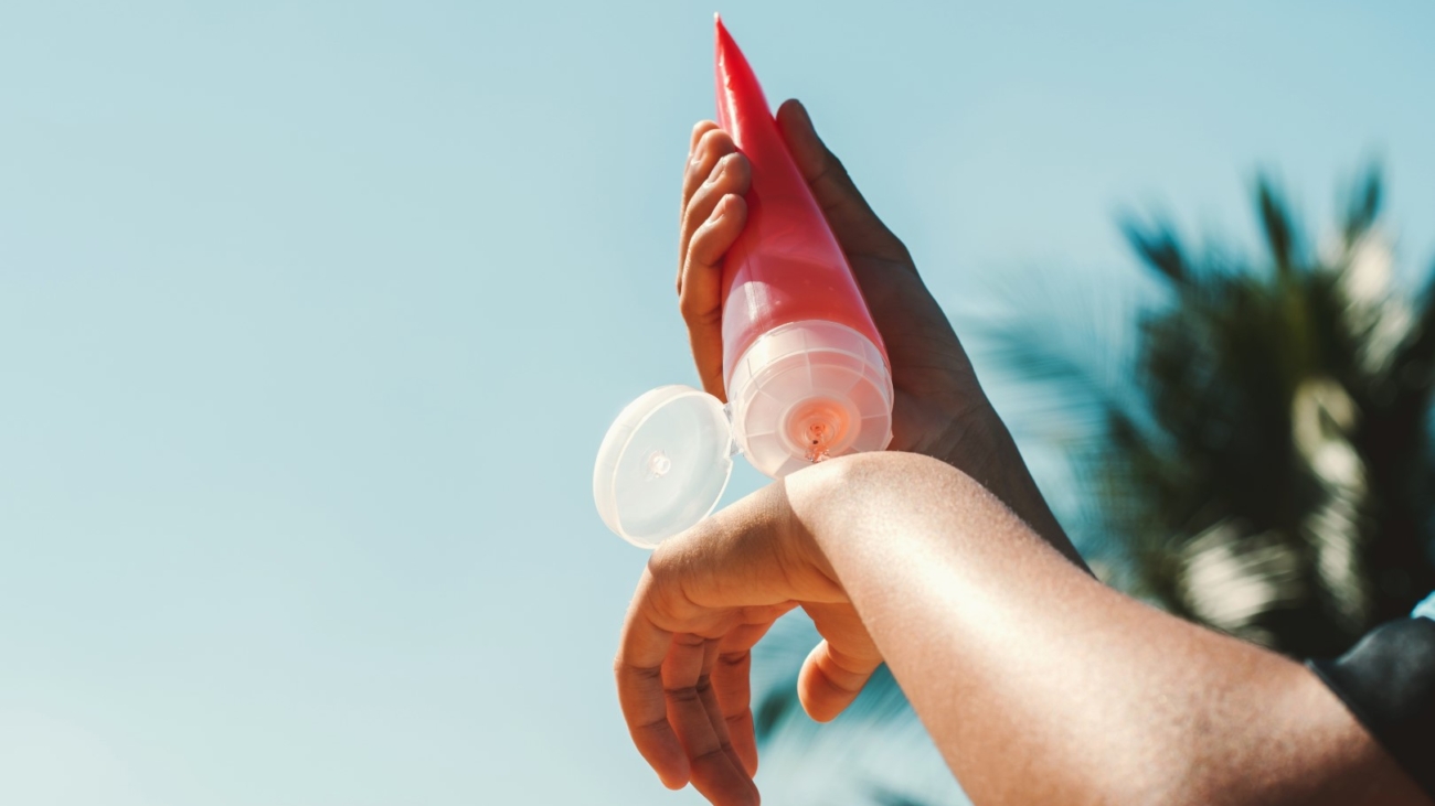 close up young woman applying sunscreen lotion on hand with blue sky background