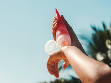 close up young woman applying sunscreen lotion on hand with blue sky background