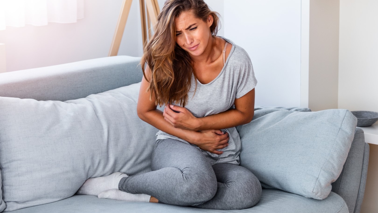 Woman lying on sofa looking sick in the living room. Beautiful young woman lying on bed and holding hands on her stomach. Woman having painful stomachache on bed, Menstrual period
