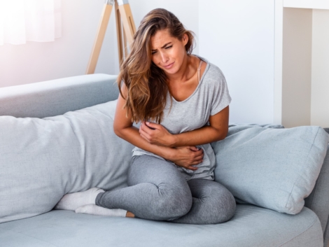 Woman lying on sofa looking sick in the living room. Beautiful young woman lying on bed and holding hands on her stomach. Woman having painful stomachache on bed, Menstrual period