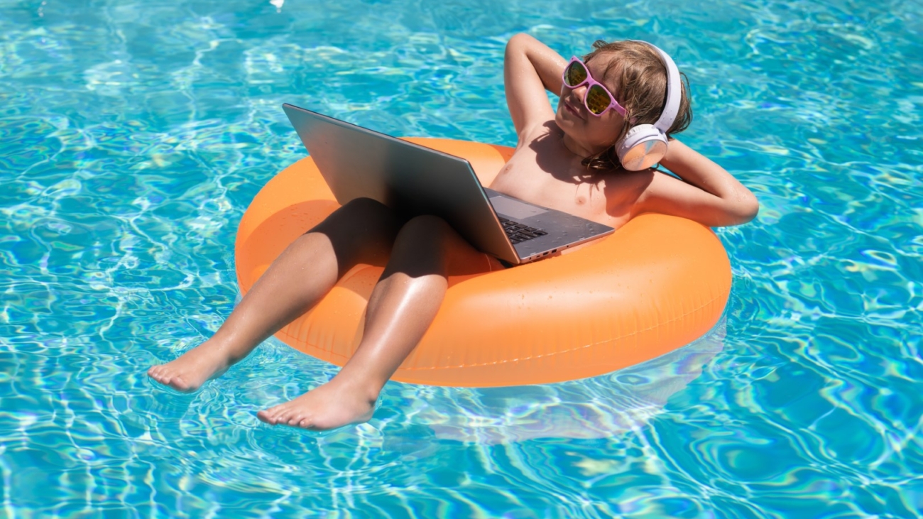 Freelance work, distance online work, e-learning. Kid working on laptop computer at poolside swimming pool. Summer online technology. Traveler relaxing on tropical sea in summer holidays