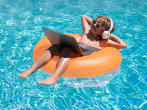 Freelance work, distance online work, e-learning. Kid working on laptop computer at poolside swimming pool. Summer online technology. Traveler relaxing on tropical sea in summer holidays